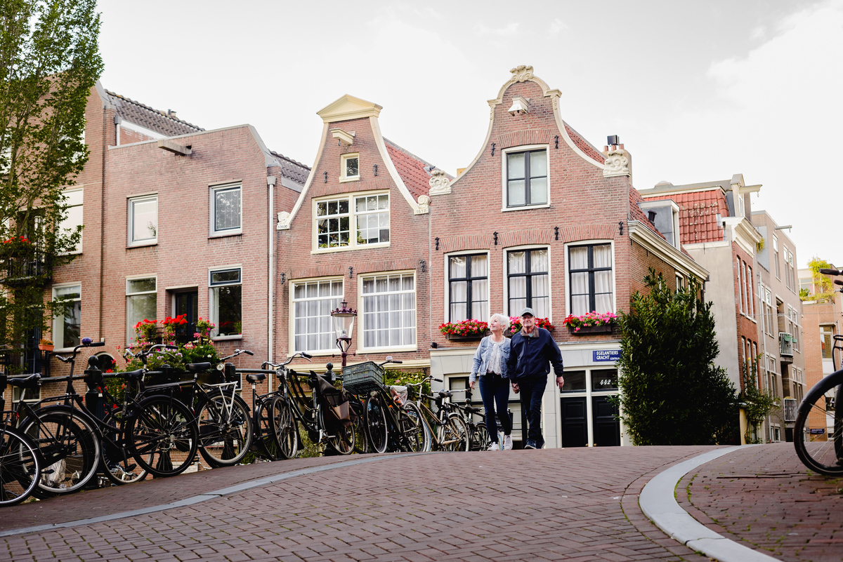 Couple standing together beside a canal house wall, calm residential street setting with classic architecture.