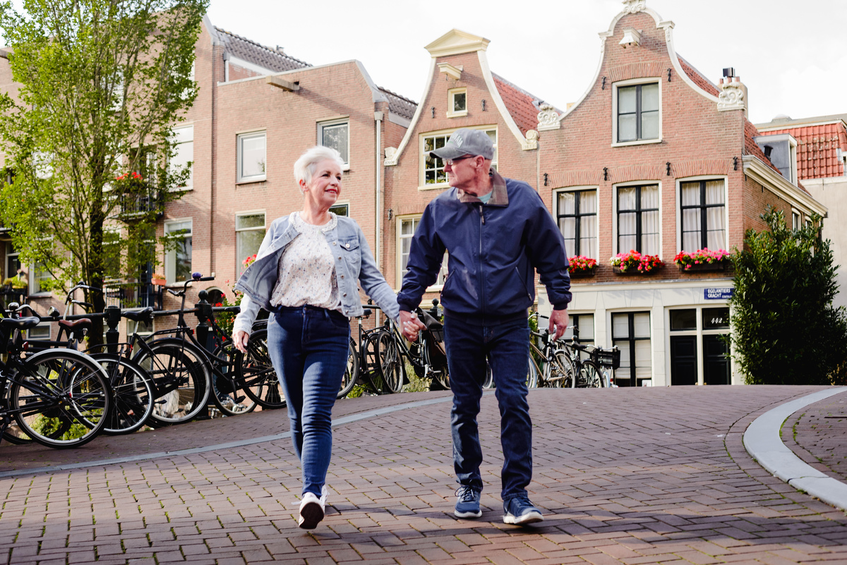 Couple walking hand in hand over a small Amsterdam bridge with historic canal houses and parked bicycles in the background.