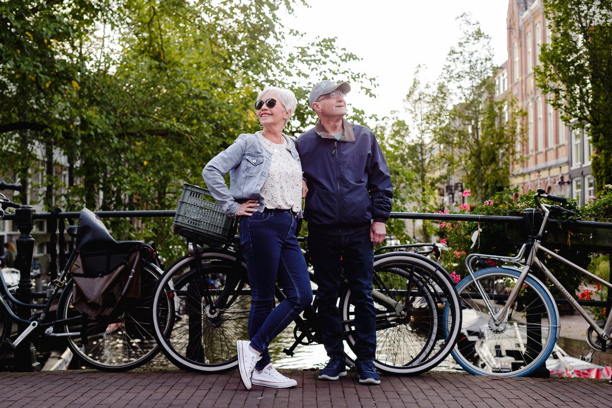 Anniversary couple posing together on an Amsterdam canal bridge surrounded by bikes, trees, and classic canal houses.