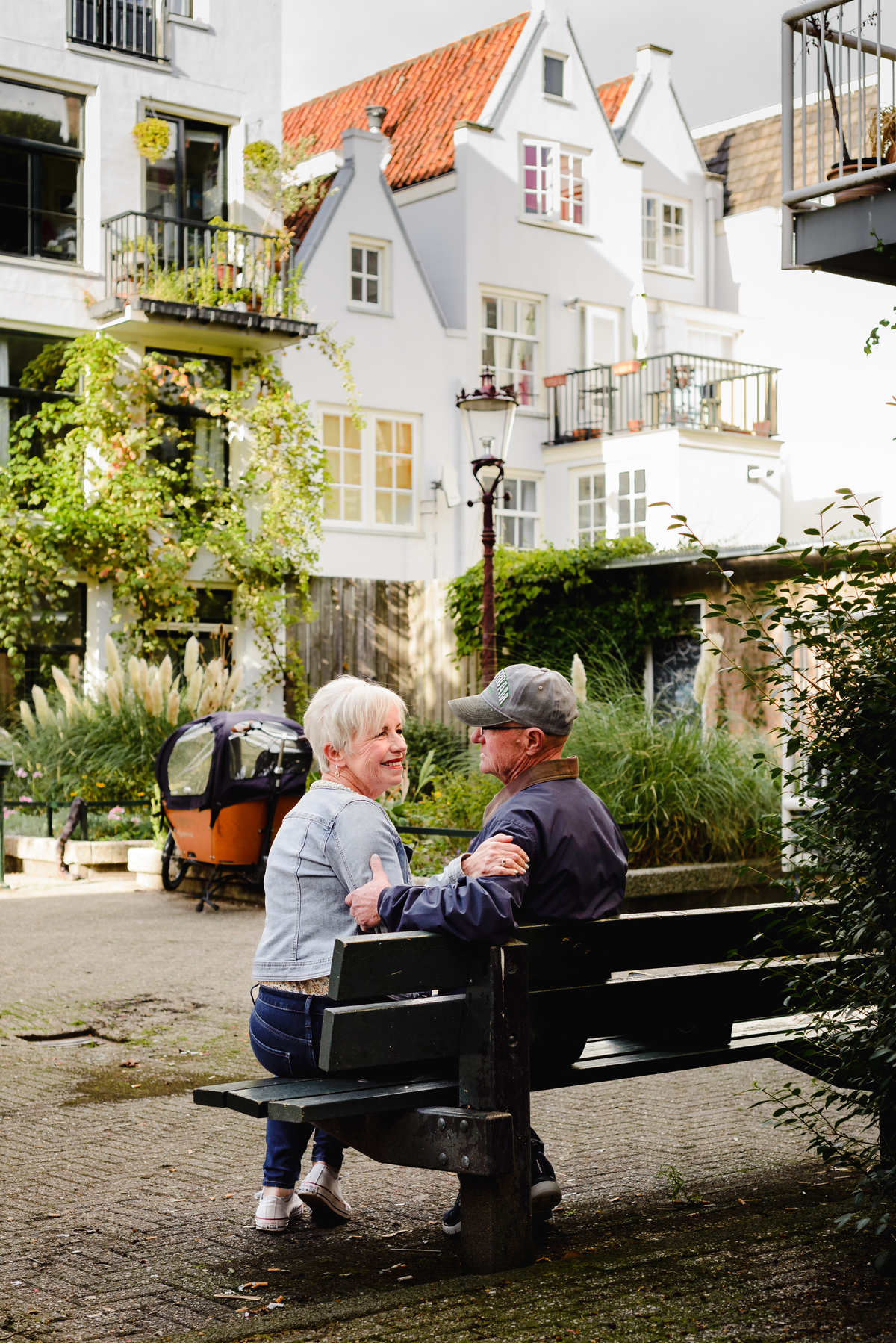 Romantic moment of an older couple sitting on a bench in Amsterdam, facing each other with soft afternoon light.