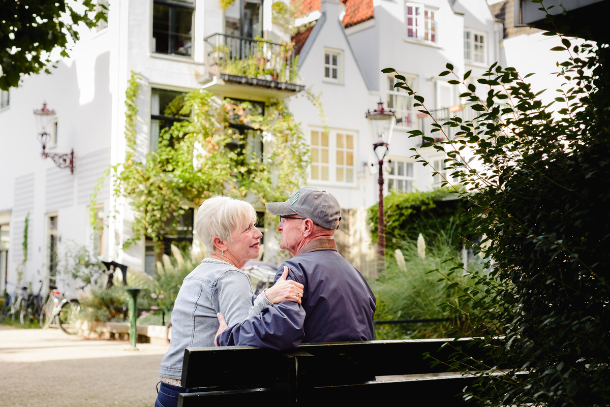 Couple sharing a quiet conversation on a bench in an Amsterdam residential area with ivy, plants, and canal houses nearby.