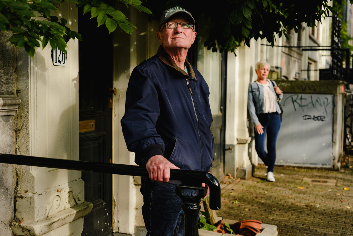 Man standing in soft sunlight near a historic Amsterdam doorway during an anniversary photo session, woman in the background.