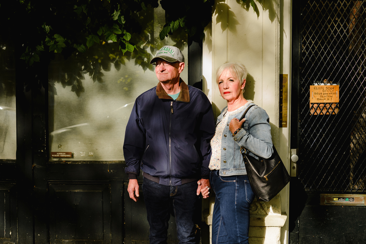 Anniversary couple standing close together against an Amsterdam building facade with dramatic light and shadows.