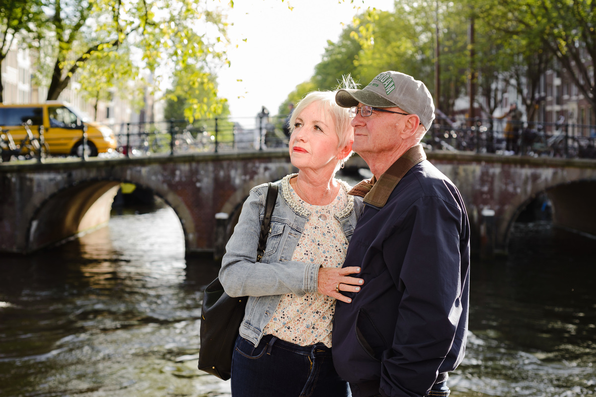 Romantic anniversary portrait of a couple standing near a canal bridge in Amsterdam, soft afternoon light and trees around.