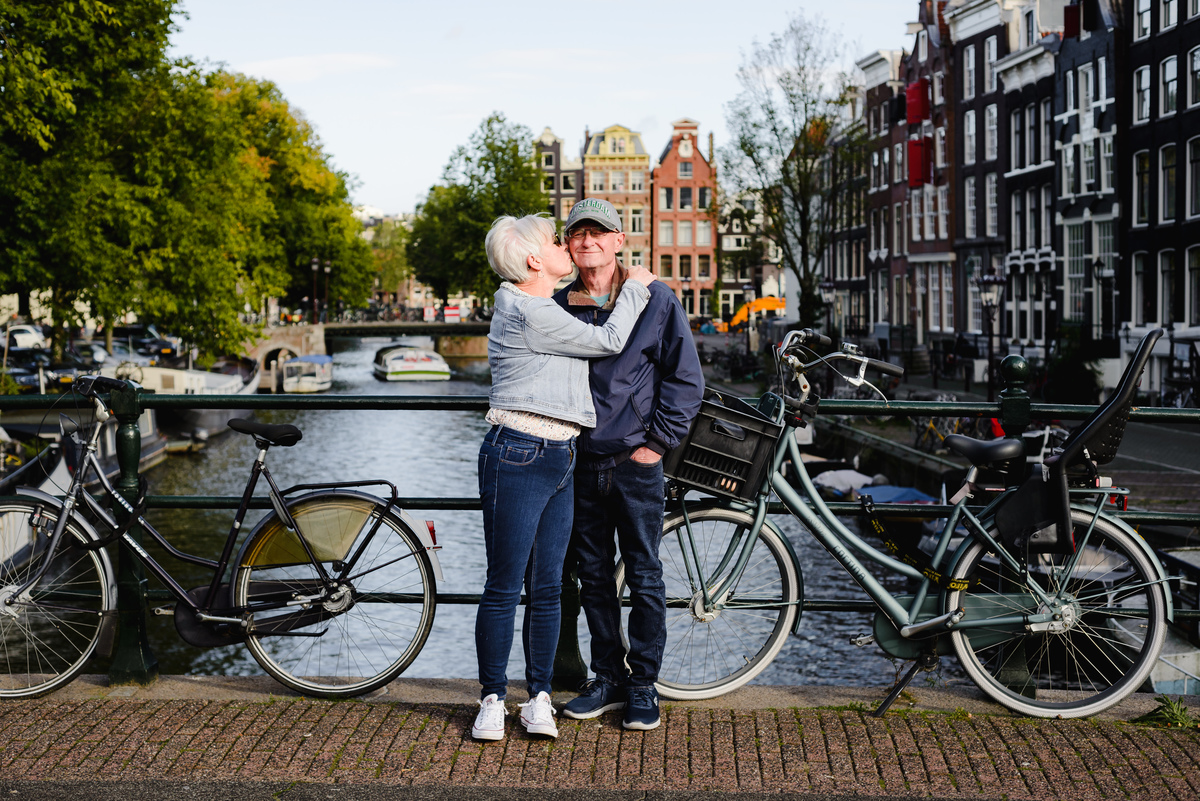 Romantic anniversary portrait of a couple standing near a canal bridge in Amsterdam, soft afternoon light and trees around.