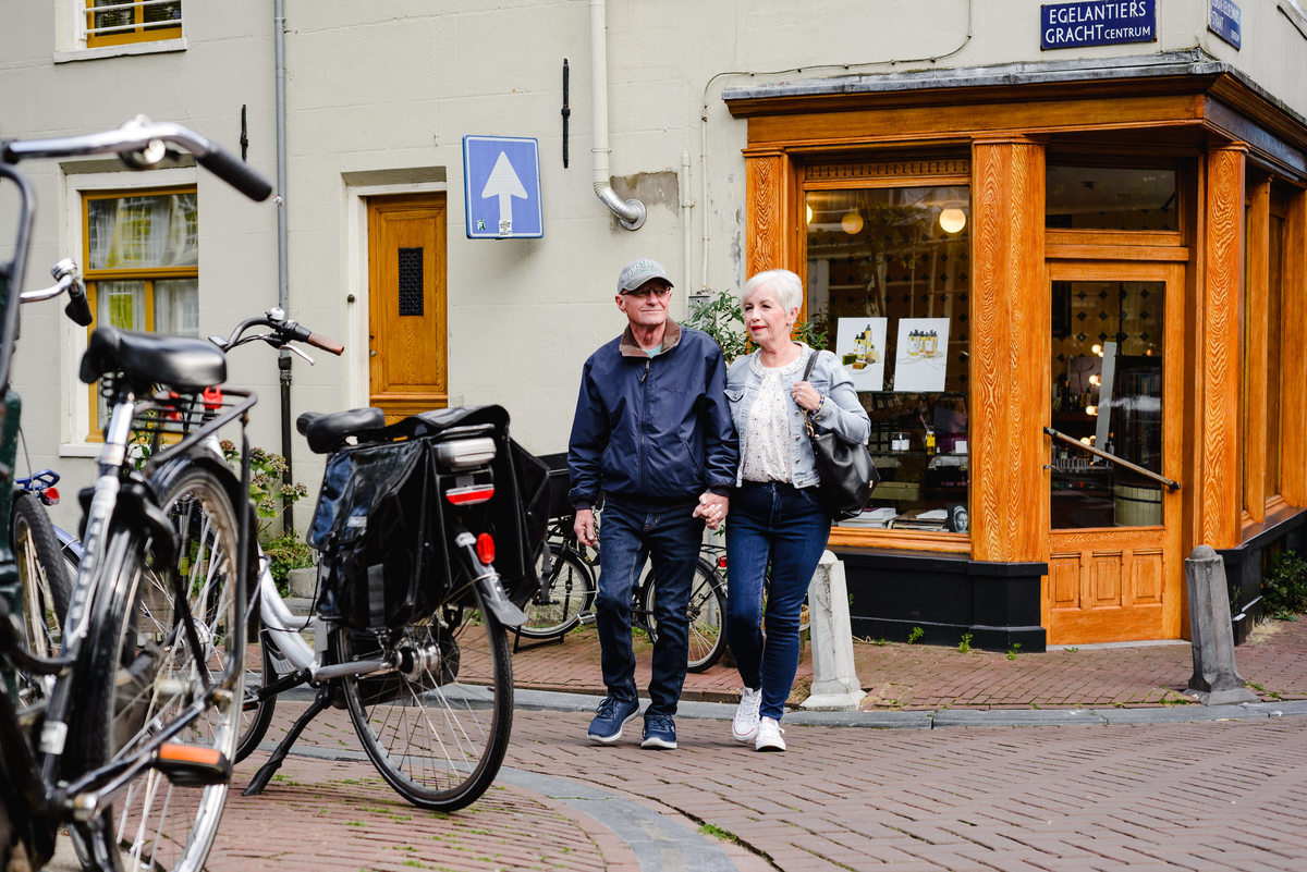 Anniversary couple walking together through a residential Amsterdam street, surrounded by trees and parked bicycles.
