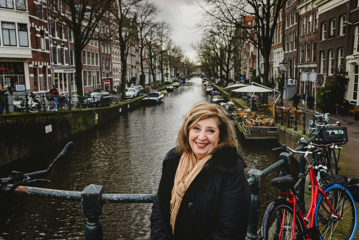 Woman smiling on an Amsterdam canal bridge during a birthday photo session, with canal houses and bicycles in the background.