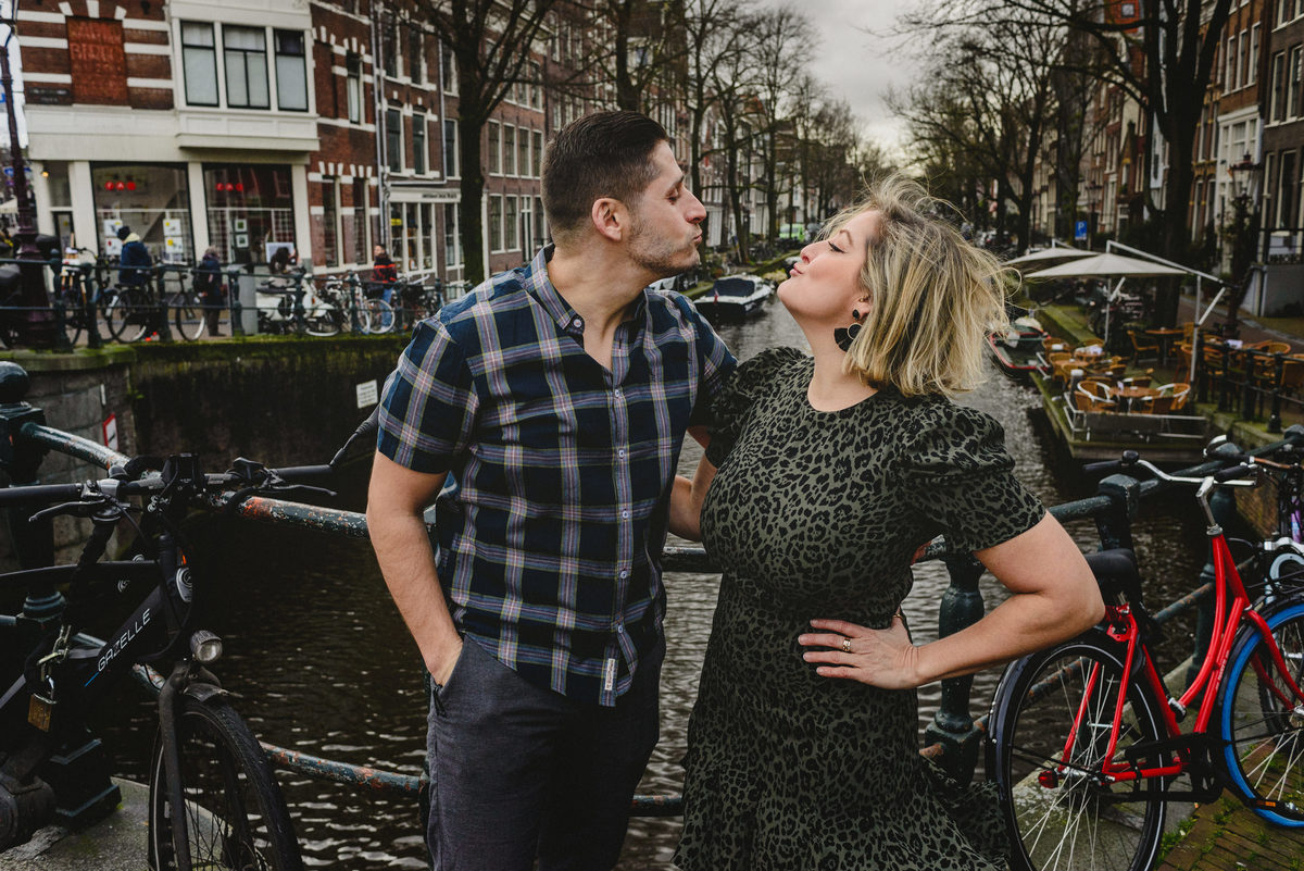 Adult siblings sharing a playful moment on an Amsterdam canal bridge, leaning toward each other during a guided photo session.