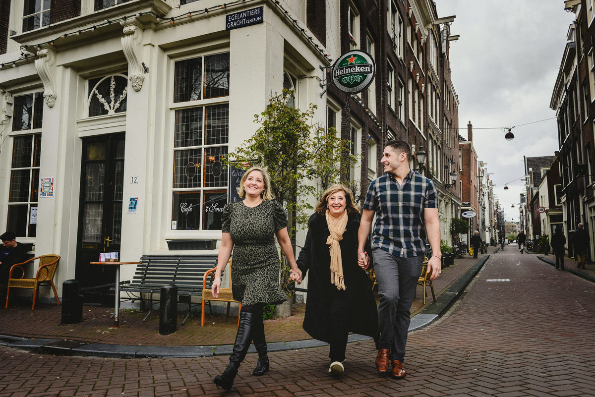 Family of three walking hand in hand along a quiet Amsterdam street, photographed during a birthday family session.