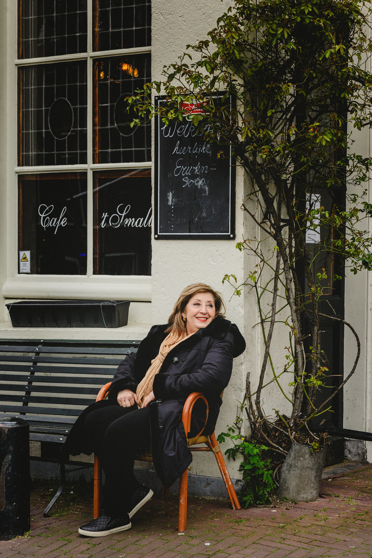 Woman seated outside a café in Amsterdam during her birthday photo session, relaxed and smiling.