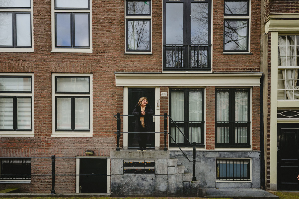 Woman celebrating her birthday in Amsterdam, posing alone in front of   a brick facade of a traditional Amsterdam house during a winter photo session.