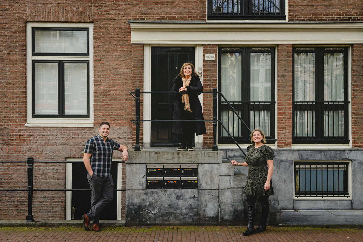 Woman celebrating her birthday in Amsterdam, posing with two adult siblings in front of a brick facade of a traditional Amsterdam house during a winter photo session.