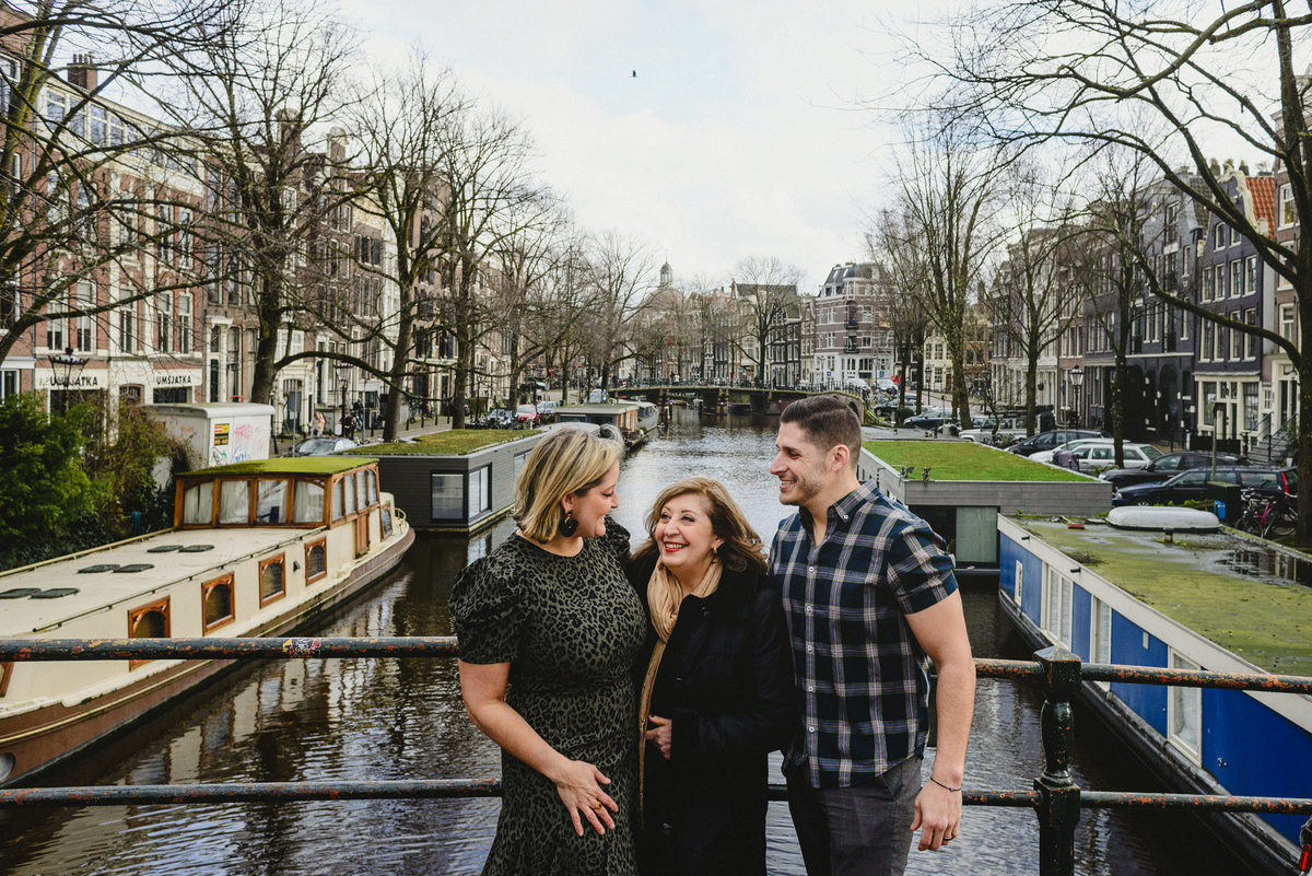 Relaxed family portrait of adult siblings and their mother in Amsterdam, photographed on a quiet canal bridge.