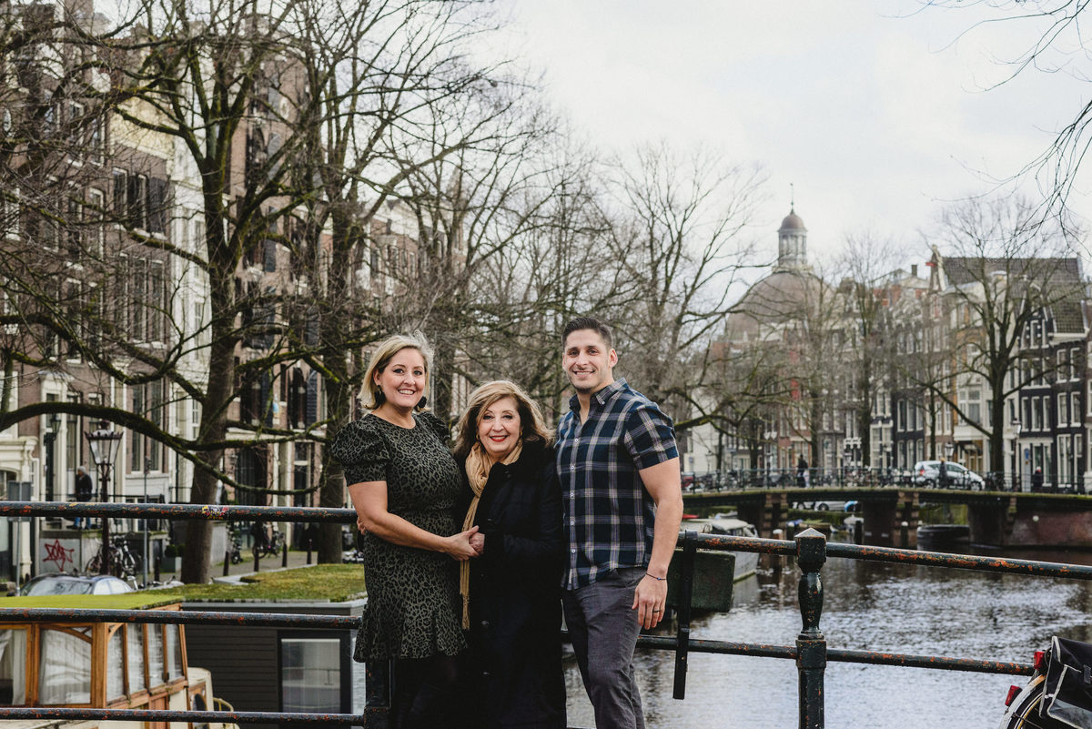 Relaxed family portrait of adult siblings and their mother in Amsterdam, photographed on a quiet canal bridge.