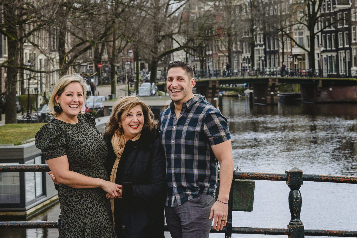 Relaxed family portrait of adult siblings and their mother in Amsterdam, photographed on a quiet canal bridge.