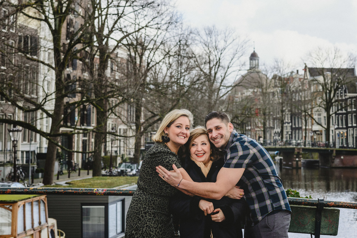 Relaxed family portrait of adult siblings and their mother in Amsterdam, photographed on a quiet canal bridge.