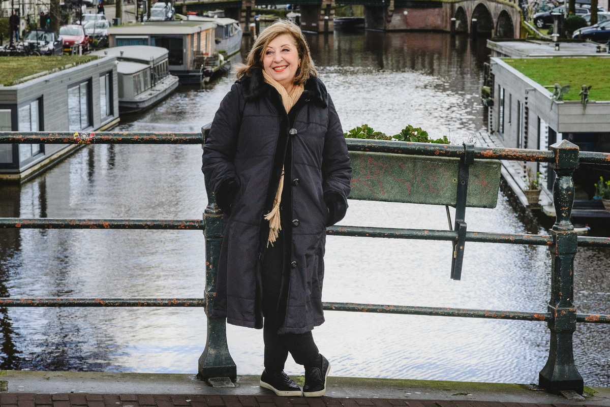 Woman smiling on an Amsterdam canal bridge during a birthday photo session, with canal houses and bicycles in the background.