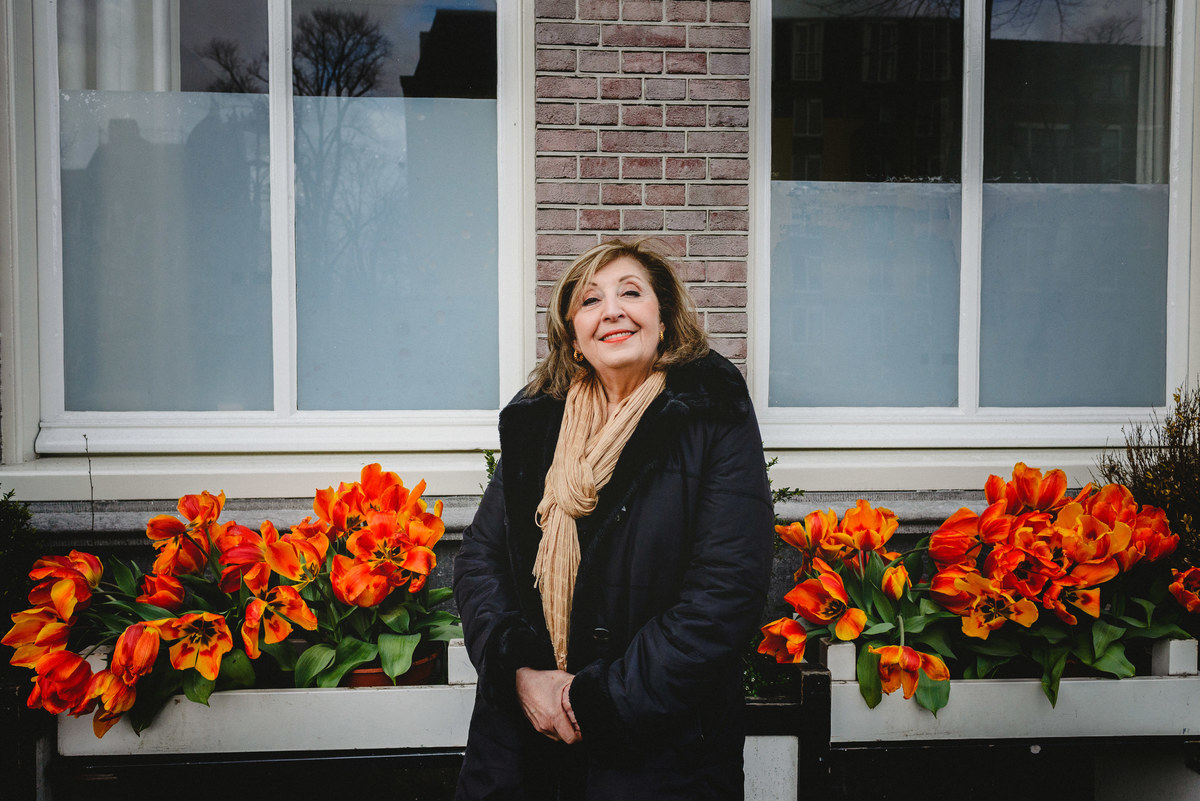 Woman celebrating her birthday in Amsterdam, posing alone in front of orange tulips and a brick facade during a winter photo session.