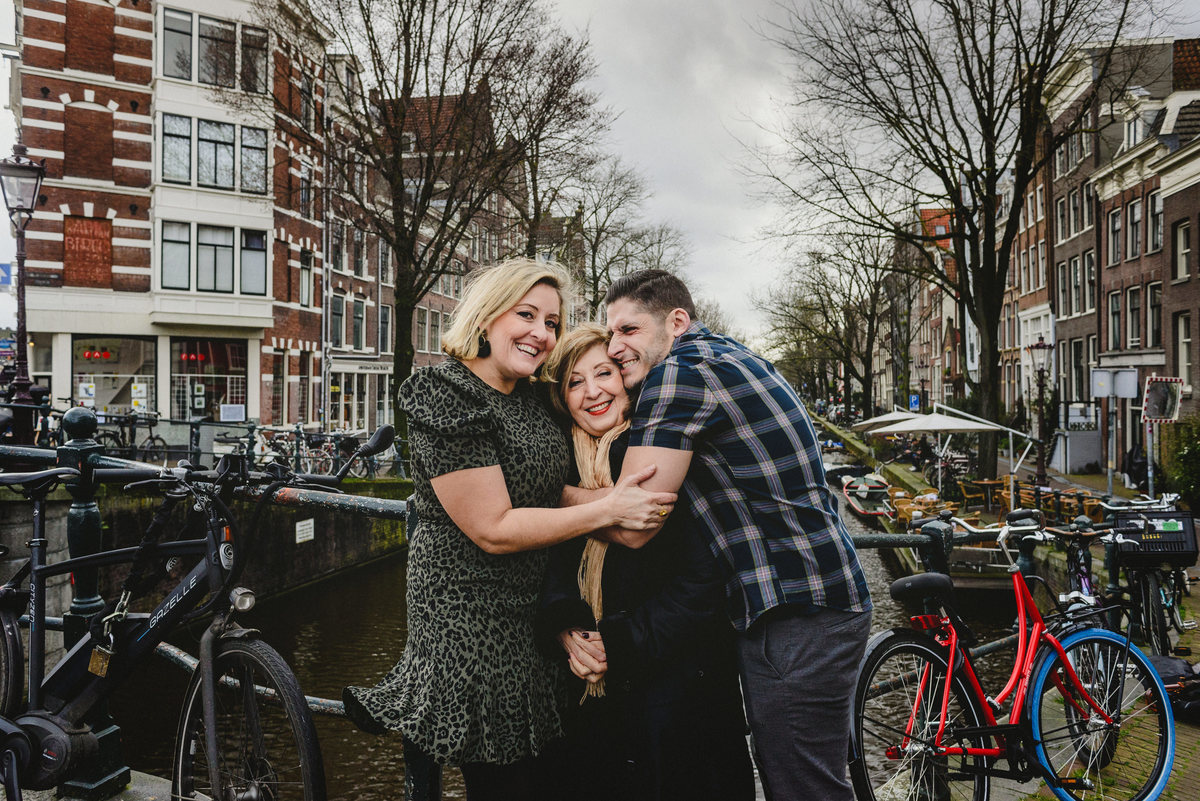 Relaxed family portrait of adult siblings and their mother in Amsterdam, photographed on a quiet canal bridge.