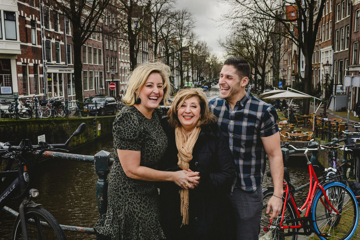Mother and adult children sharing a joyful moment on a canal bridge in Amsterdam, captured in a posed but natural style.