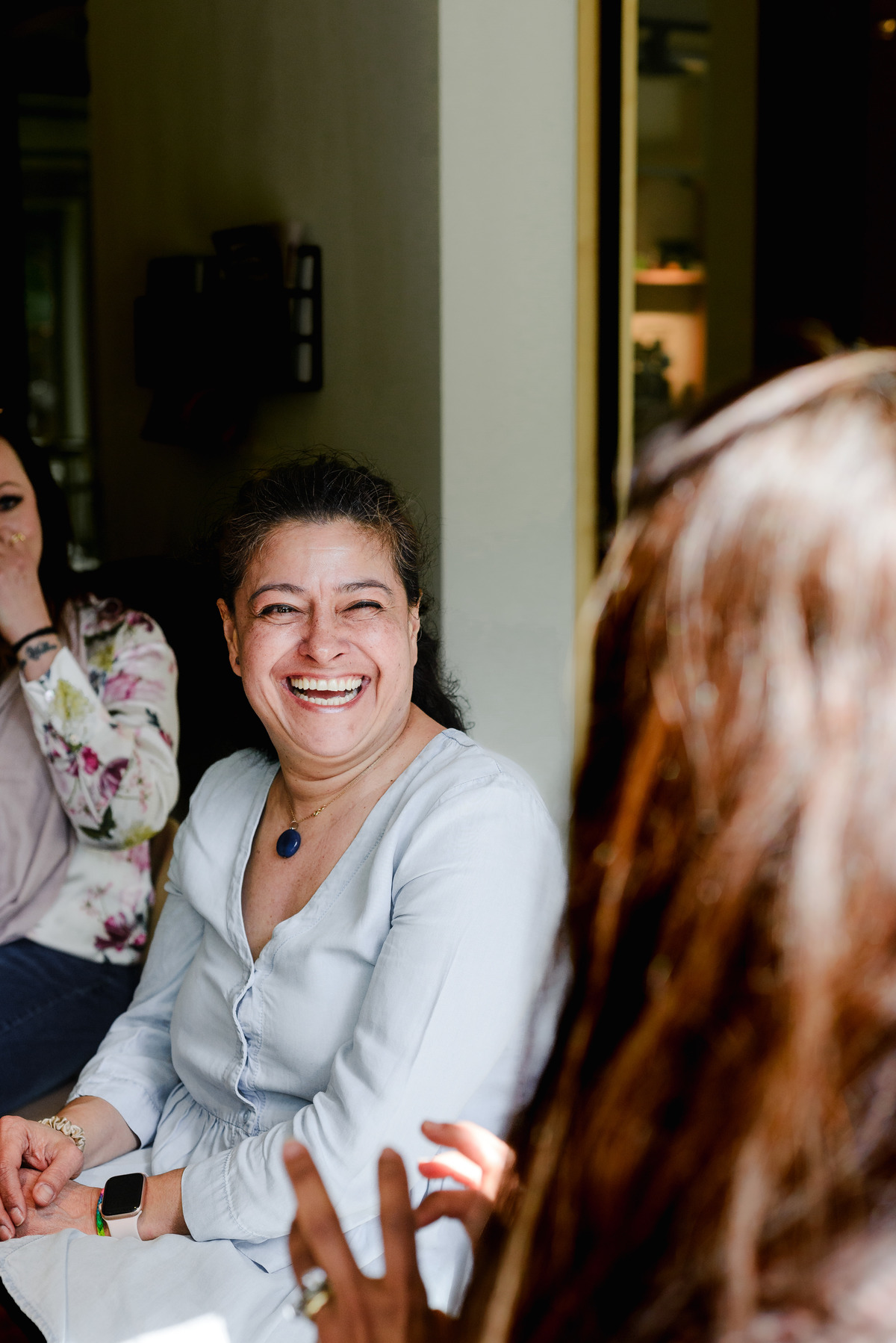 Woman smiling and laughing during a relaxed brunch gathering, seated at a shared table indoors.