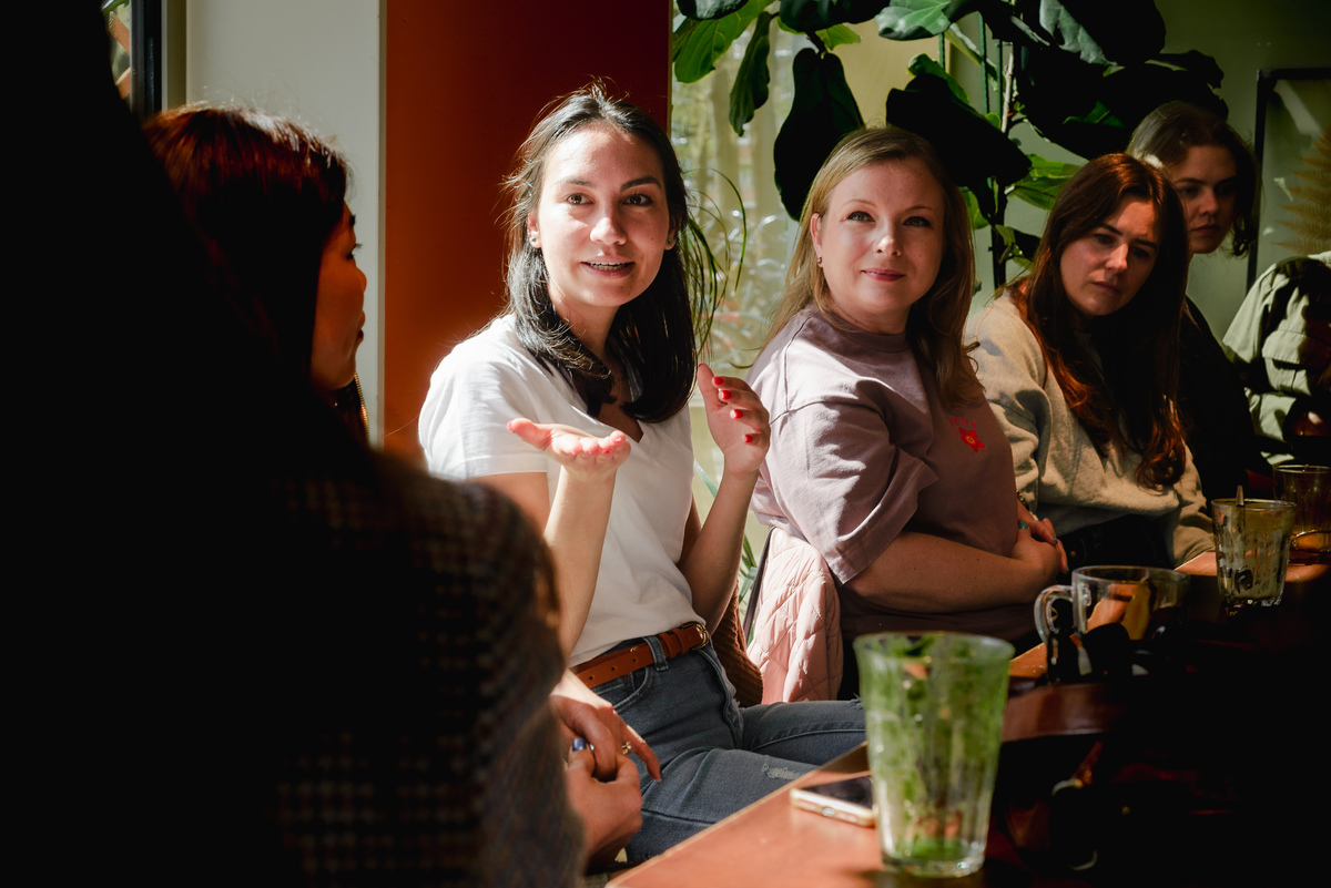 Woman speaking and gesturing during a small women’s networking brunch in Amsterdam, candid group conversation.