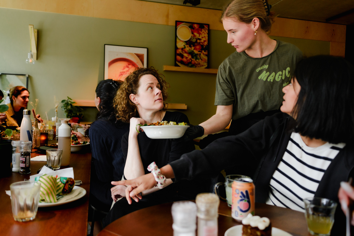 Server presenting a dish to guests at a small women’s brunch event in Amsterdam, intimate indoor setting.