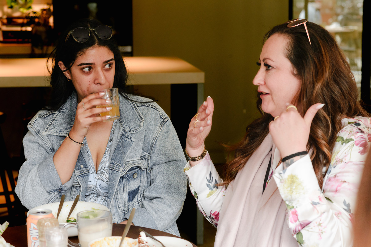 Two women talking over lunch at a community brunch, photographed with a natural event photography style.