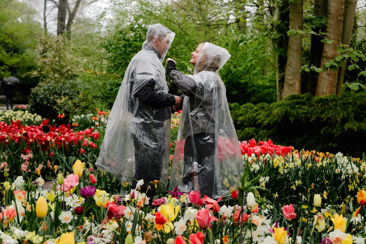 Emotional moment during a rainy proposal in Keukenhof Gardens, couple smiling at each other surrounded by tulips and spring flowers.