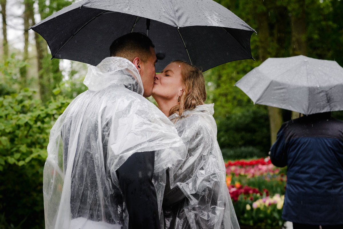 Close-up of couple kissing under an umbrella during a rainy proposal moment at Keukenhof, tulips in bloom around them.