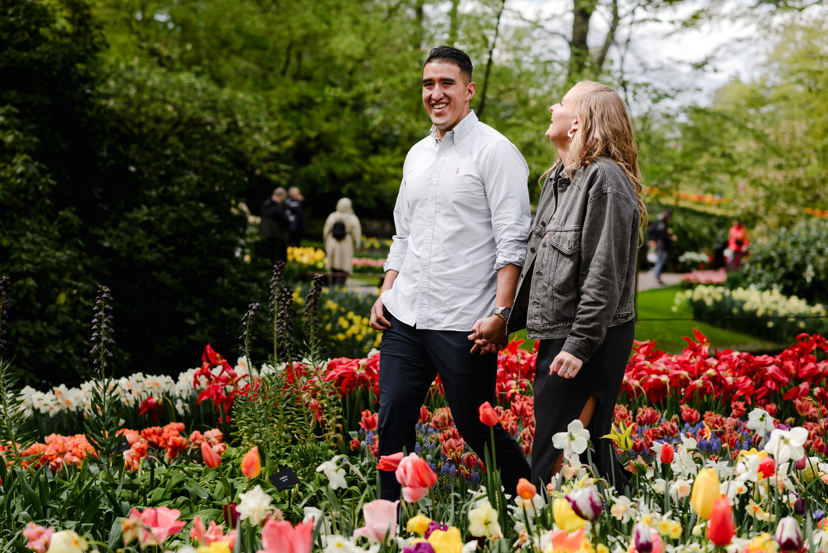 Engaged couple laughing together while walking through Keukenhof flower beds, spring blooms and trees creating a calm atmosphere.