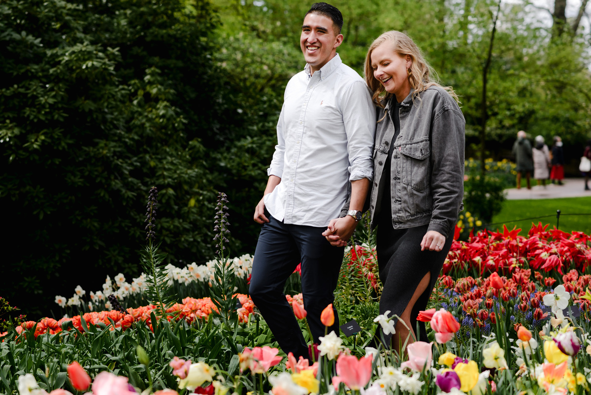 Couple holding hands and walking through Keukenhof tulip gardens after proposal, natural light and colorful flowers around them.
