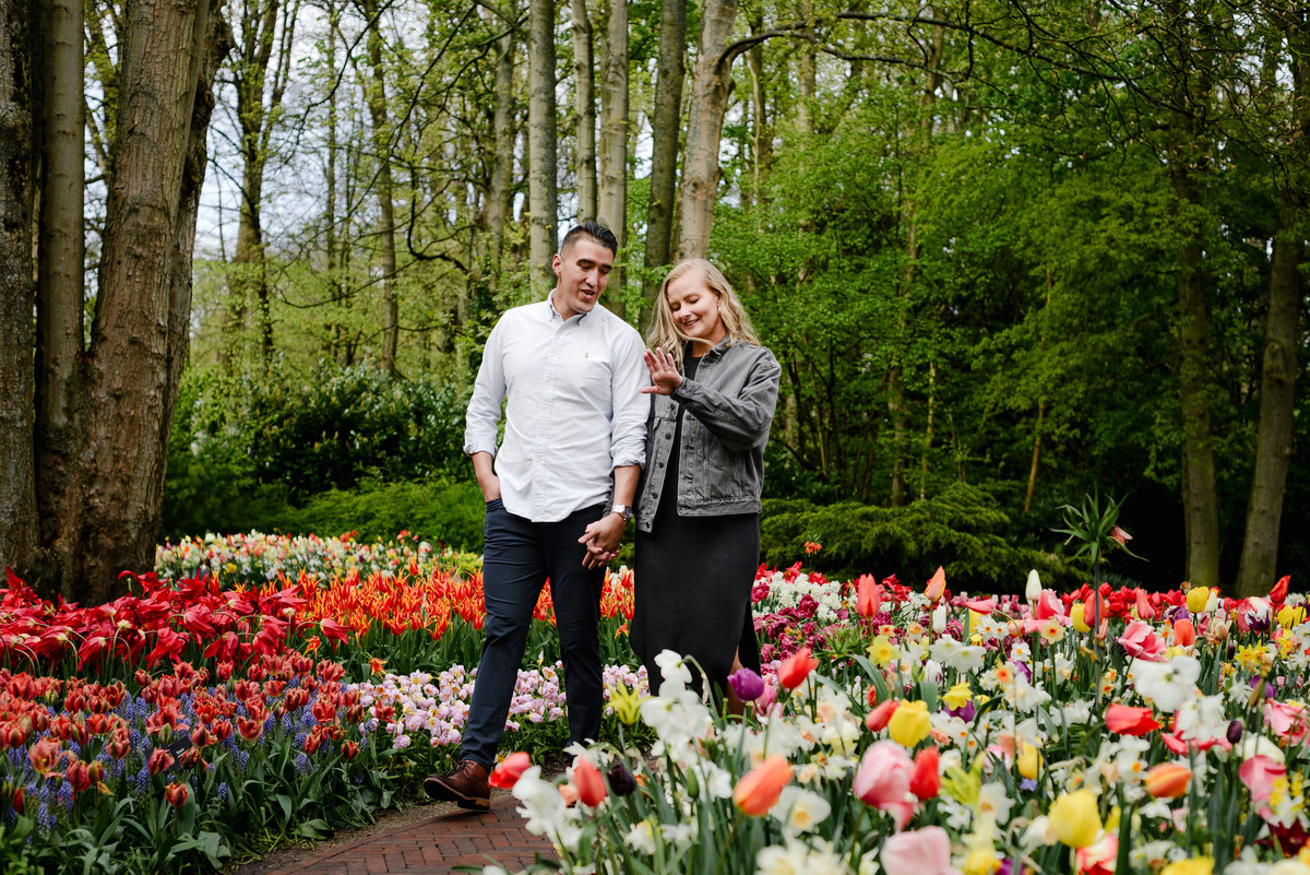 Engaged couple walking slowly through Keukenhof gardens, relaxed and smiling after proposal, tulips in full bloom.