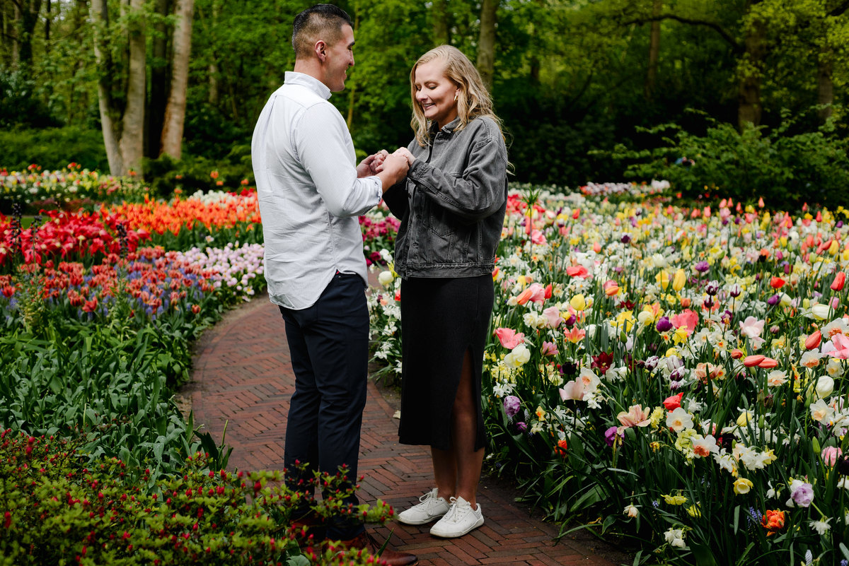Couple holding hands among tulips in Keukenhof, relaxed and smiling after a surprise proposal.