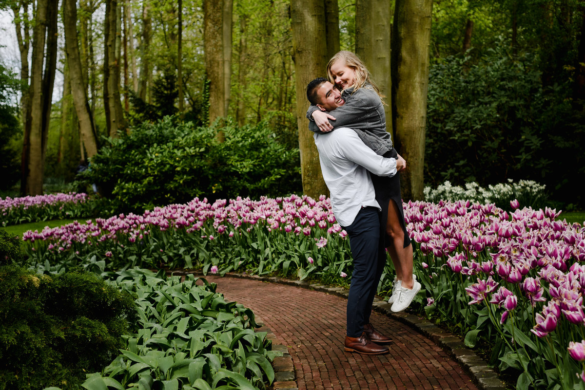 Couple enjoying a quiet walk through Keukenhof gardens after proposal, surrounded by spring flowers and tall trees.