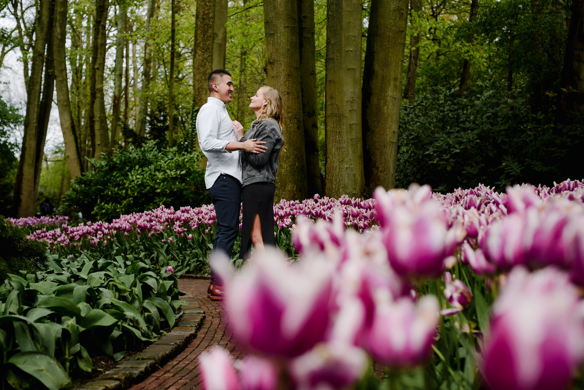 Couple enjoying a quiet walk through Keukenhof gardens after proposal, surrounded by spring flowers and tall trees.