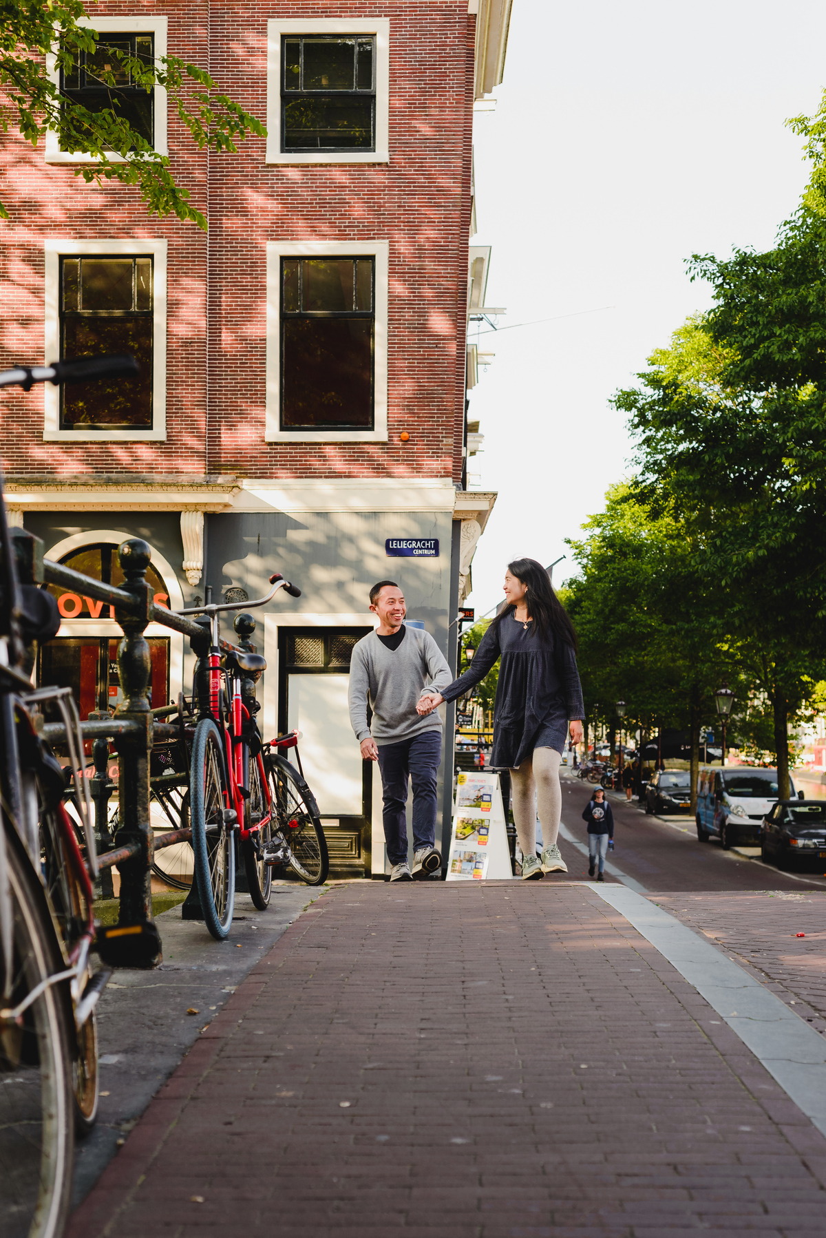Couple embracing on a bridge with classic Amsterdam canal houses and bicycles surrounding them.