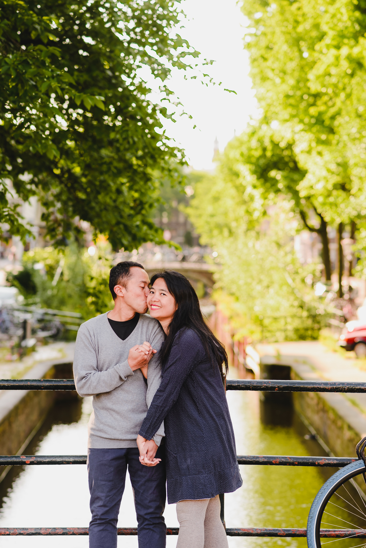 Couple walking hand in hand past historic canal houses in Amsterdam during a relaxed photo session.