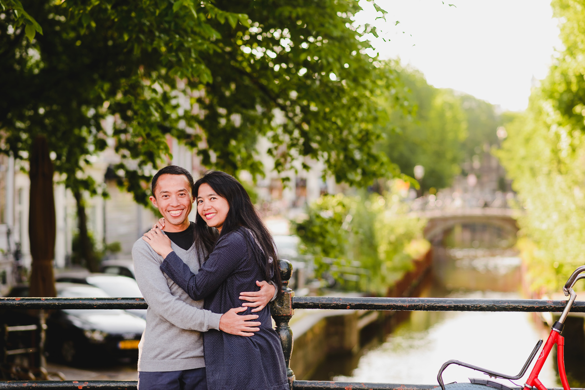 Couple standing together by a canal railing in Amsterdam, framed by classic architecture and bicycles.