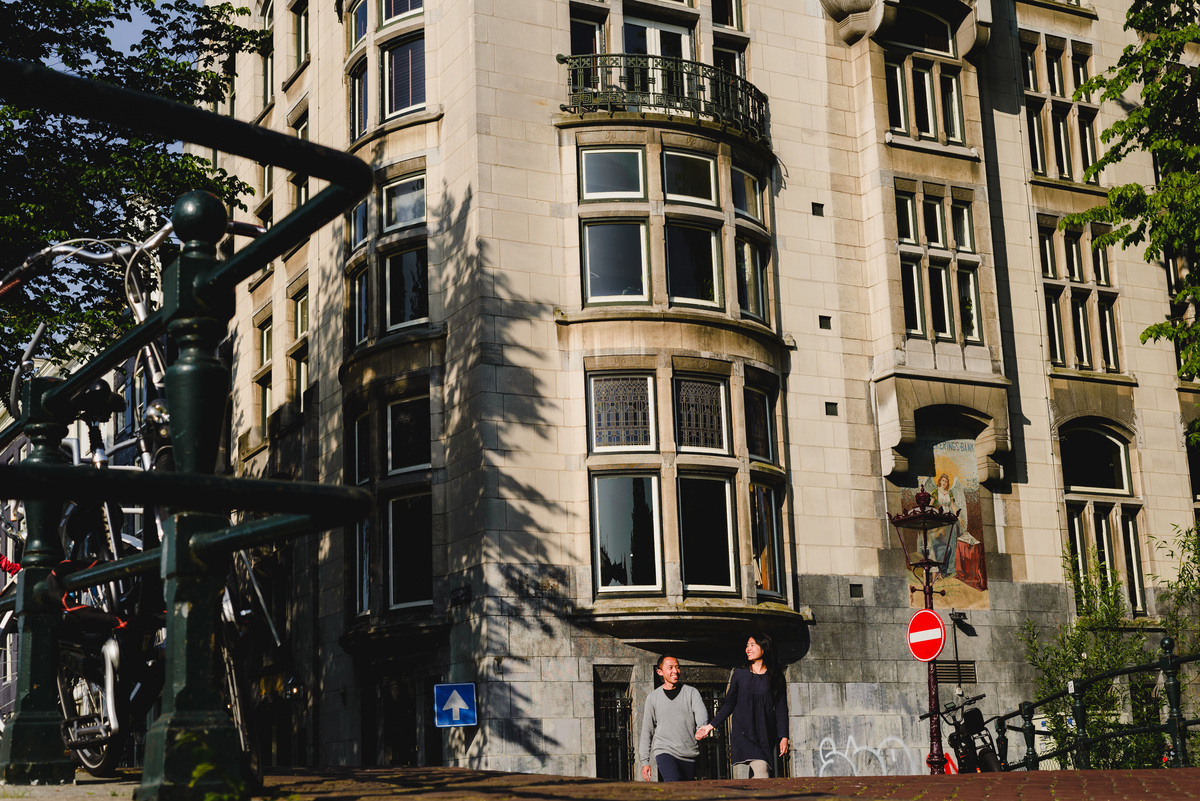 Couple holding hands while walking near a canal bridge in Amsterdam, captured in natural daylight.