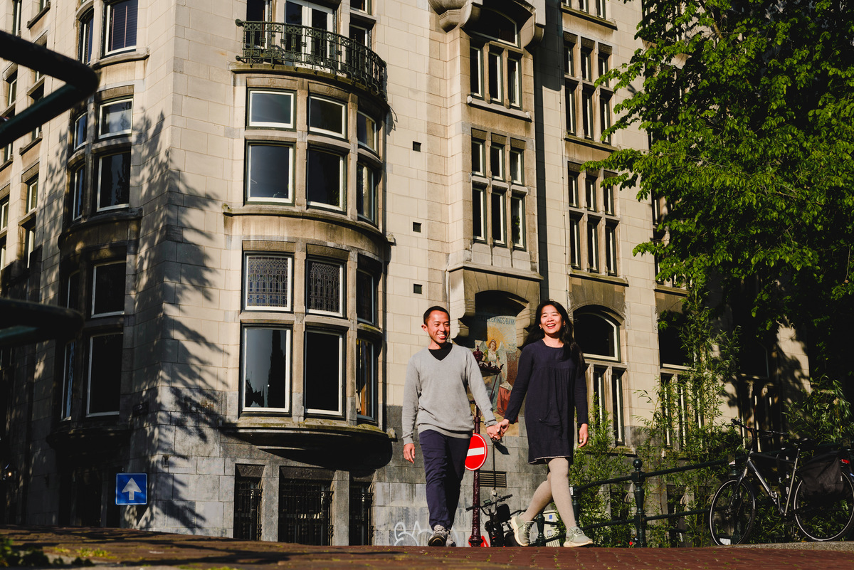 Couple posing in front of a historic corner building along an Amsterdam canal, relaxed and smiling.