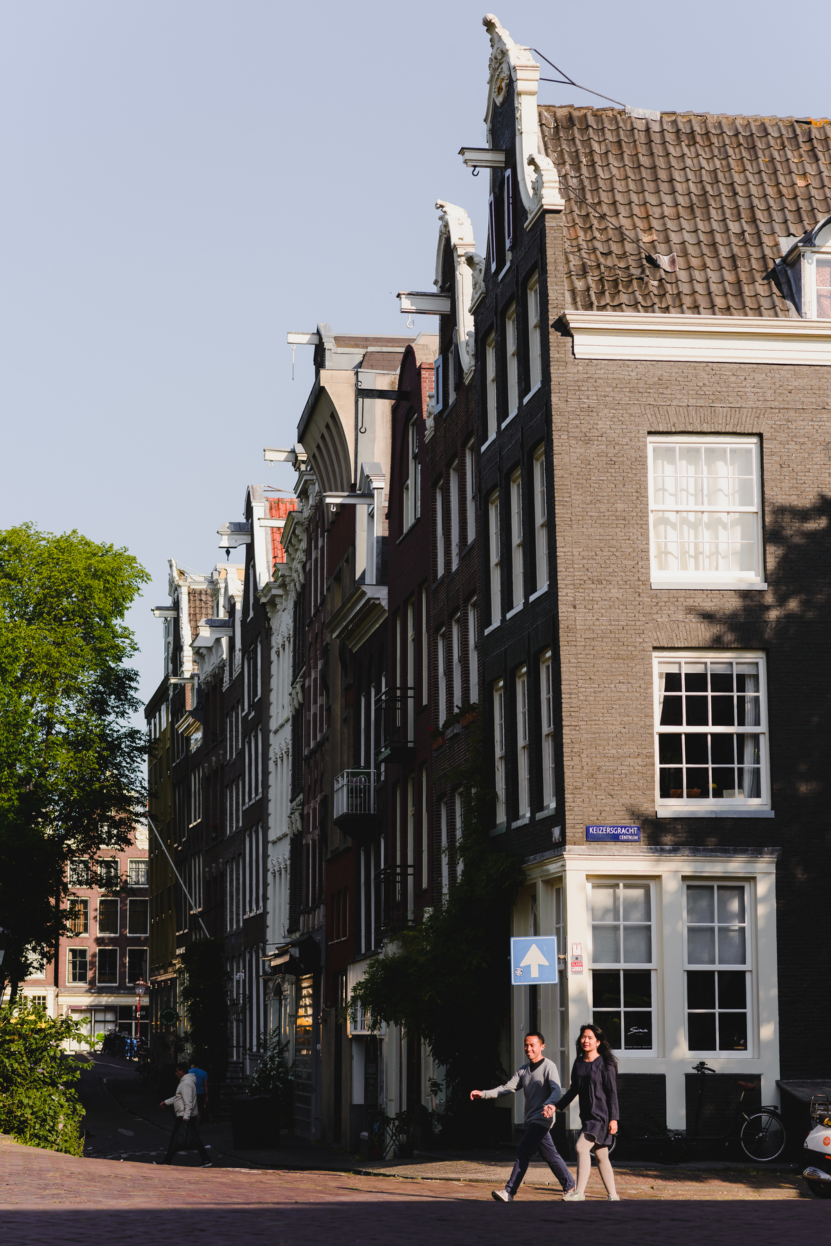 Couple embracing on a canal bridge in Amsterdam, with boats and trees creating a romantic setting.