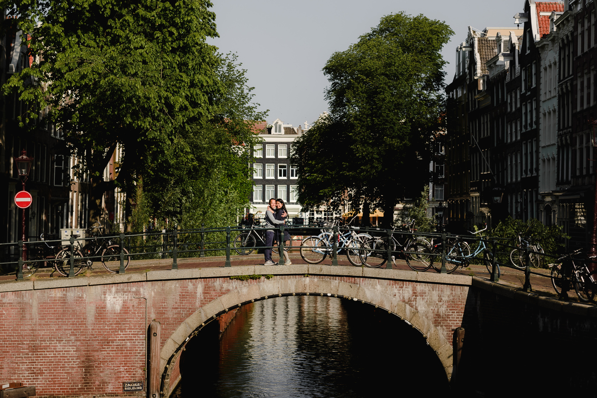 Couple sharing a quiet moment on an Amsterdam canal bridge, surrounded by greenery and calm water.