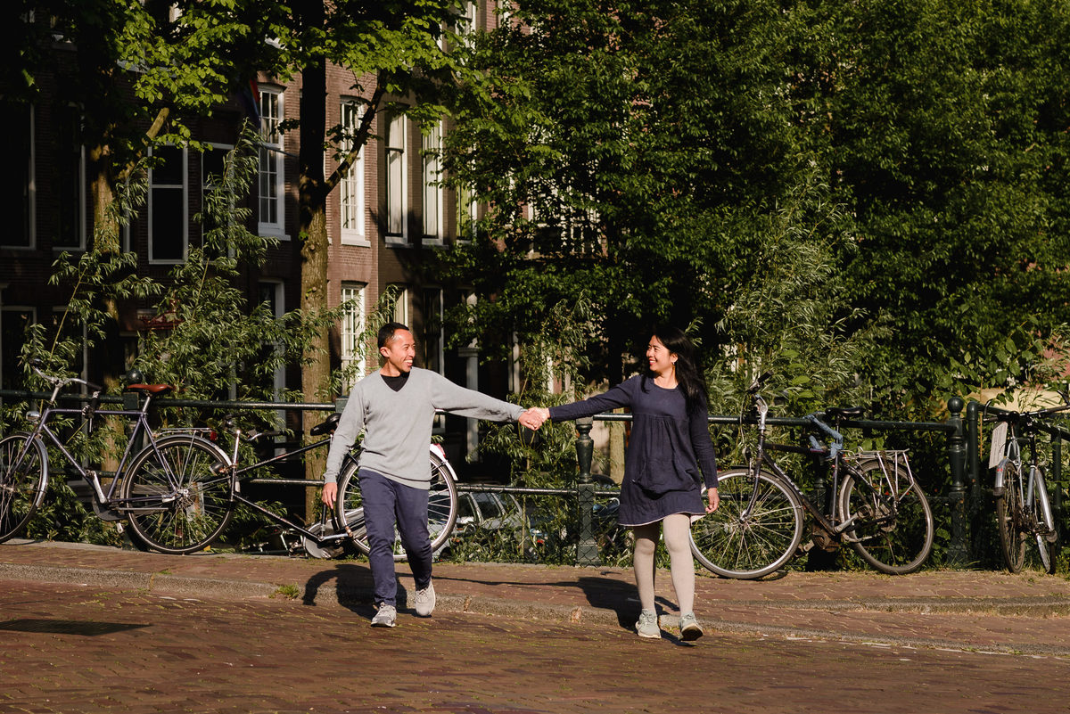 Couple holding hands while walking along a quiet Amsterdam canal street with bicycles and green trees