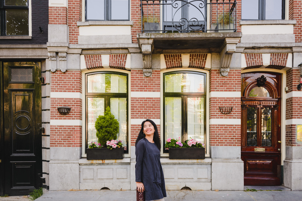 Woman standing in front of a classic Amsterdam brick house with large windows and flower boxes