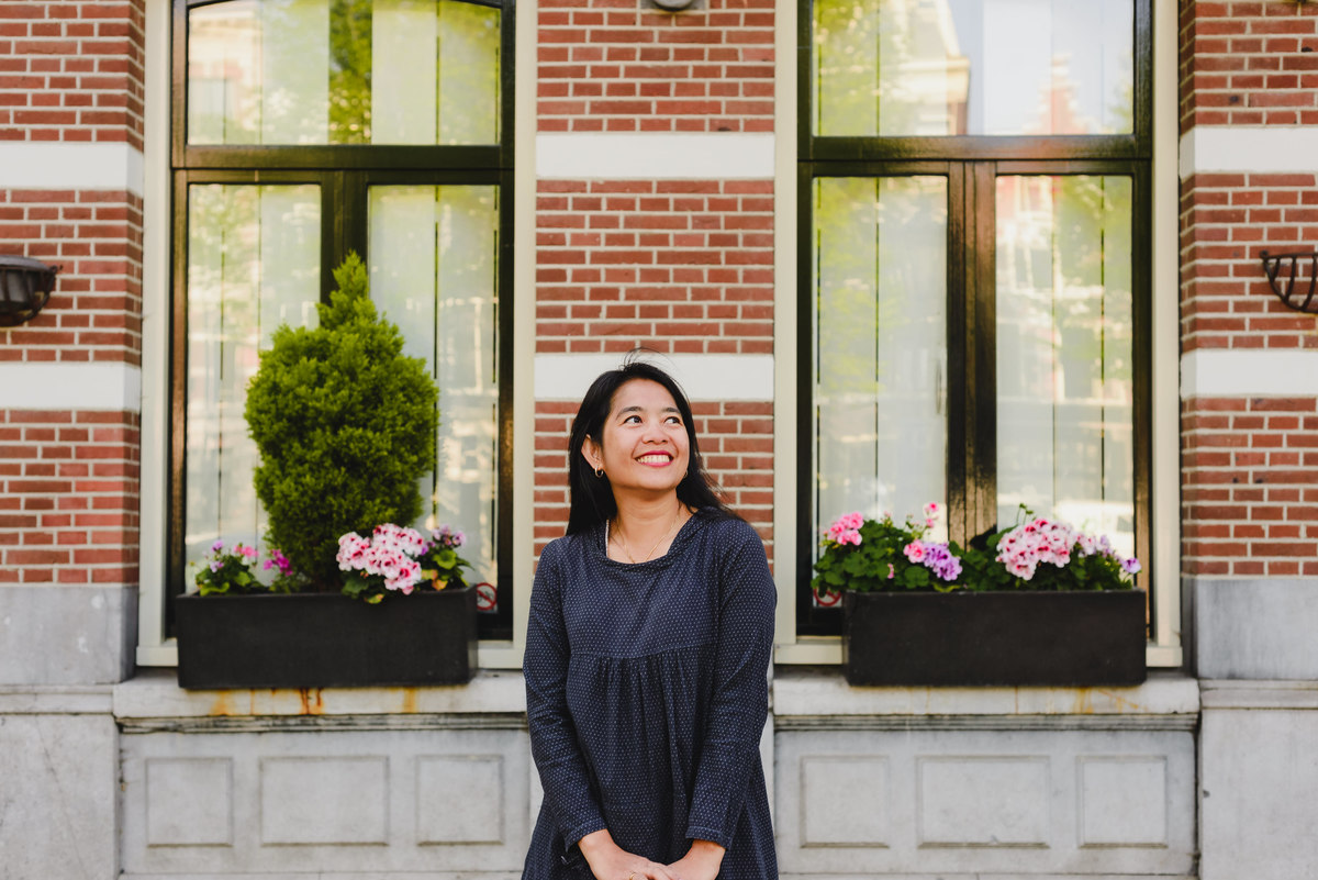 Portrait of a woman smiling in front of traditional Amsterdam canal houses with soft daylight