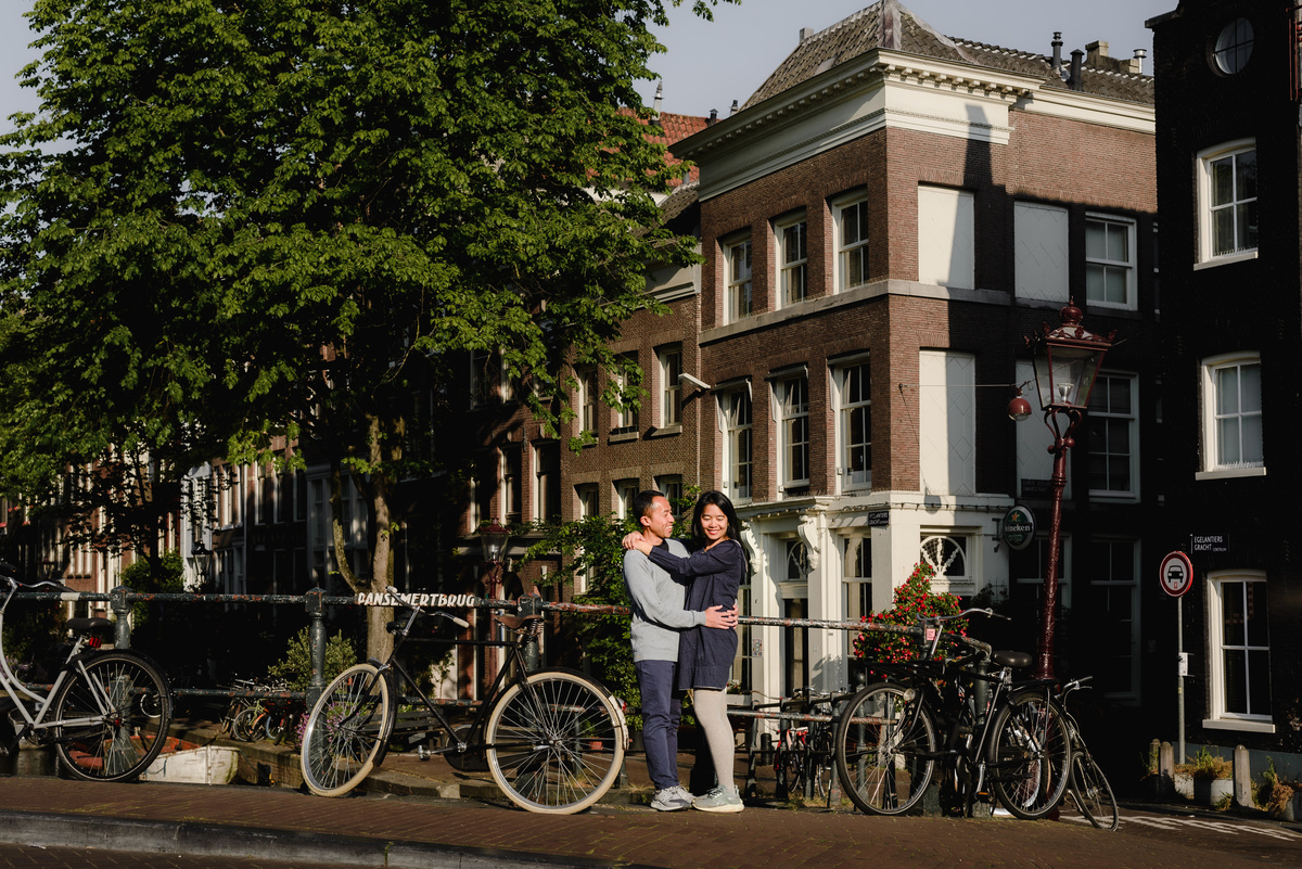 Couple walking hand in hand along an Amsterdam canal street with bicycles and historic brick buildings in the background.