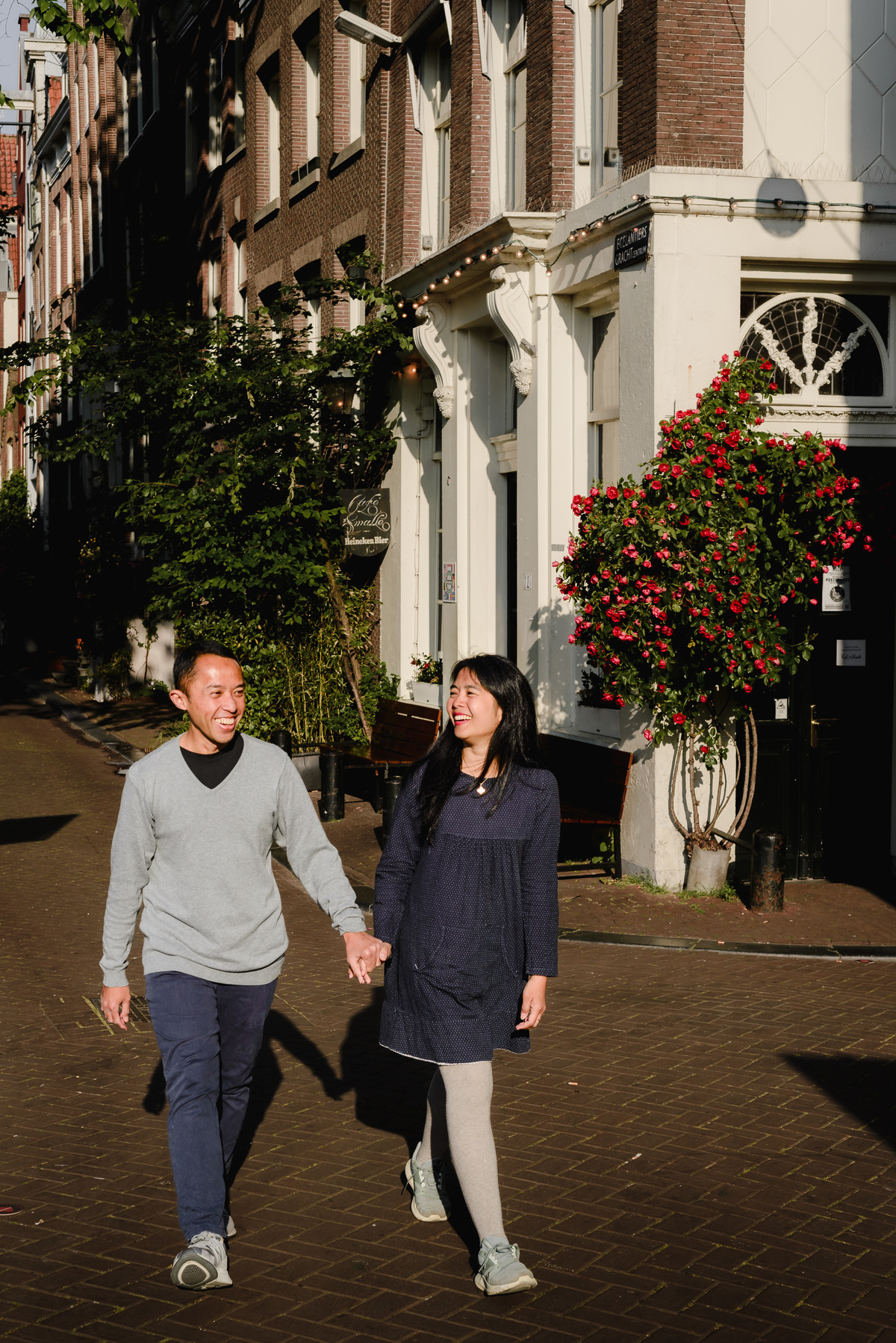 Couple walking together along a canal wall with traditional Amsterdam houses and bicycles behind them.
