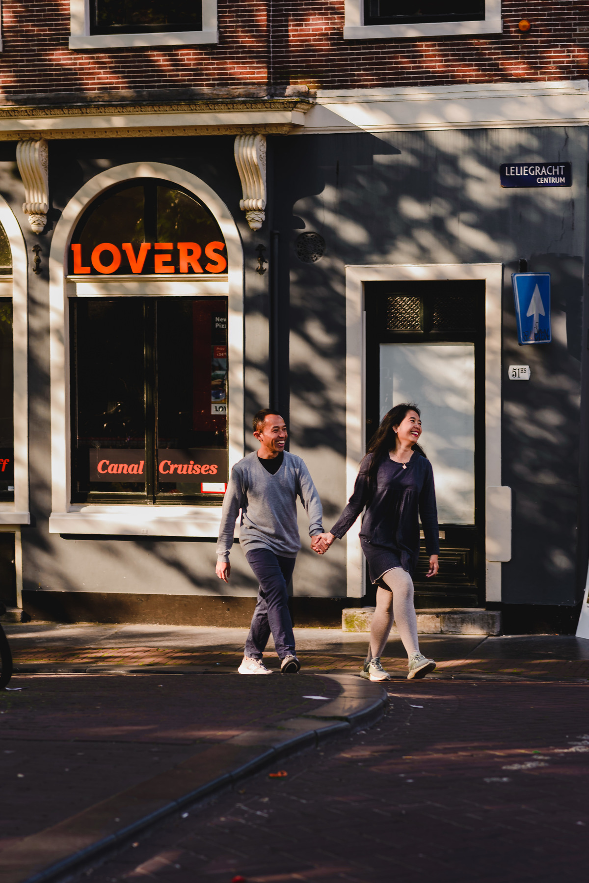 Couple sitting together on a bench beside an Amsterdam canal lined with bicycles and leafy trees.