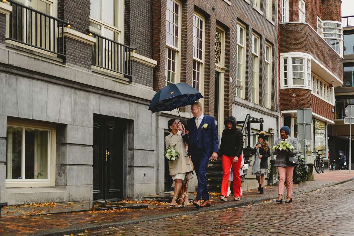 Couple walking under umbrella in light rain before civil wedding ceremony in Amsterdam